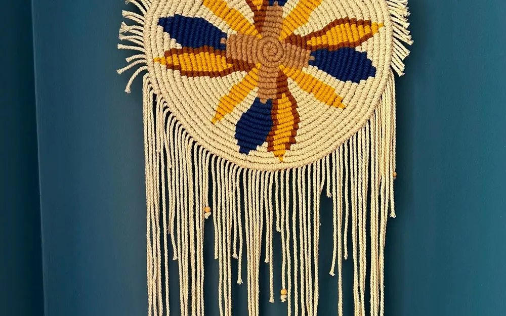 Création MAM'CRAM : attrape-rêves en macramé à motif de fleur bleue et jaune, sur fond bleu canard.